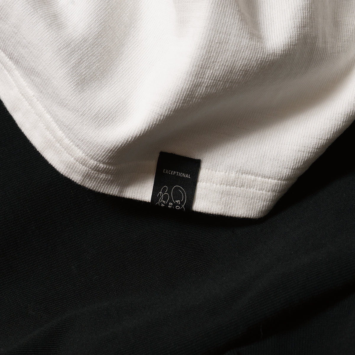 C1018 White jersey and hem label detail, photographed over dark fabric.